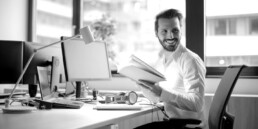 Mann sitzt lächelnd am Arbeitsplatz